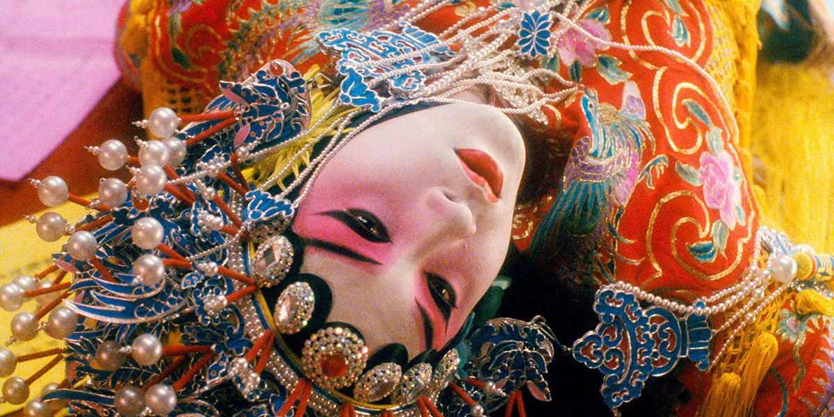 A person in makeup and colourful costume lies on their back